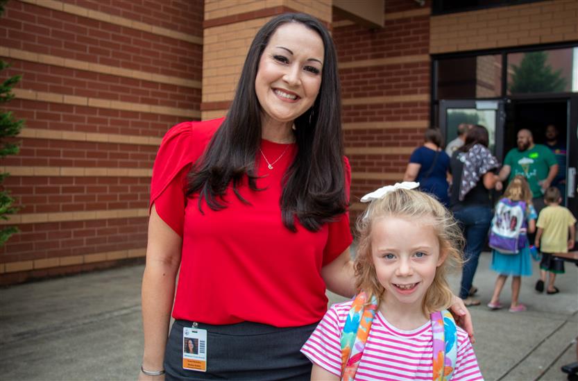 A staff member wearing a red shirt smiles with a girl wearing pink